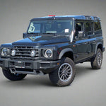 Black off-road vehicle parked on a paved surface with a building and trees in the background.