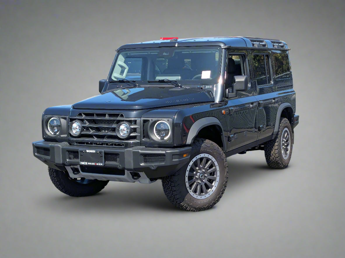 Black off-road vehicle parked on a paved surface with a building and trees in the background.