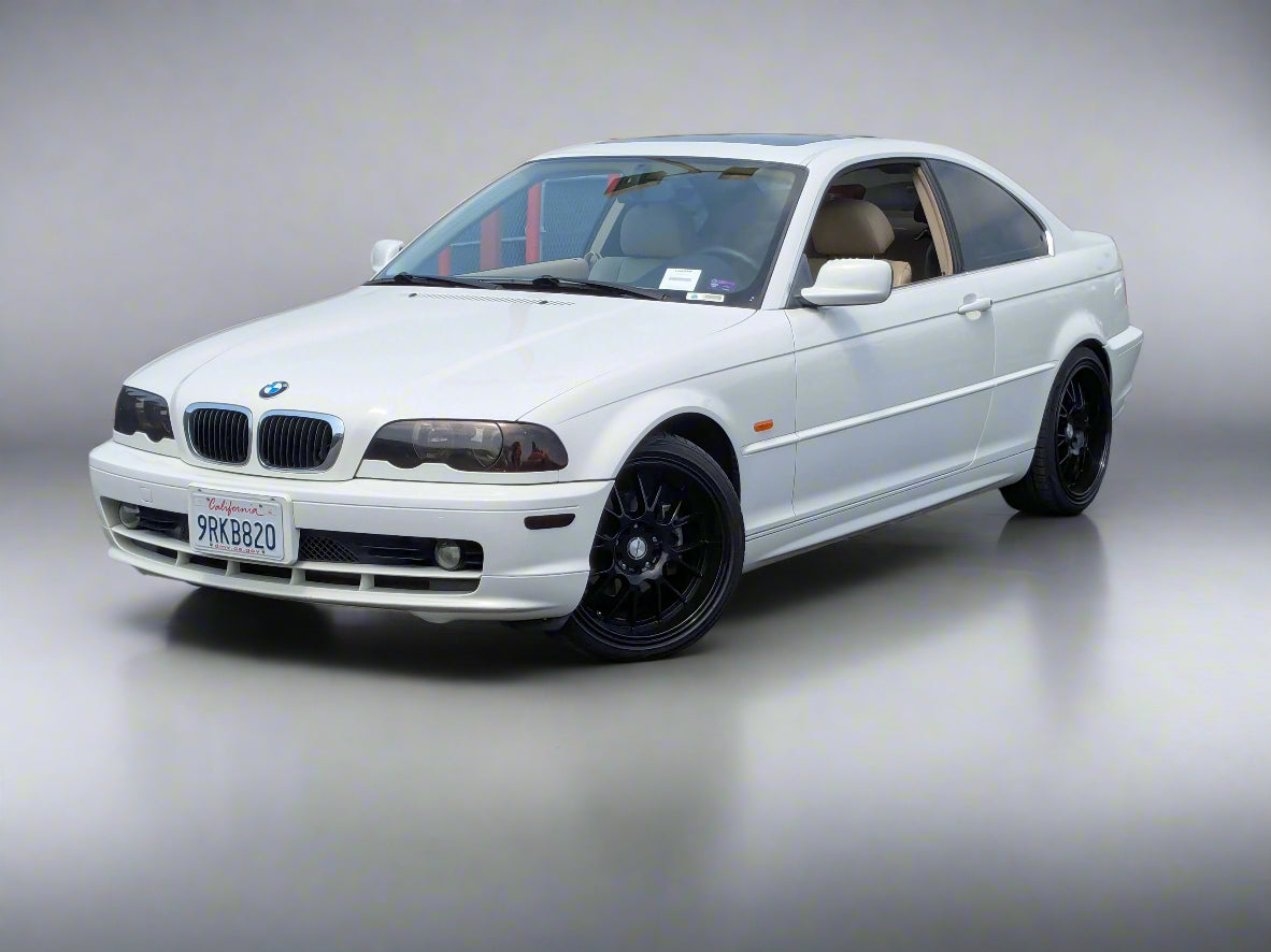 White BMW car parked in a lot with a building and fence in the background